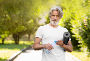 ein gesunder mann im reifen alter, er hält eine wasserflasche und yogamatte