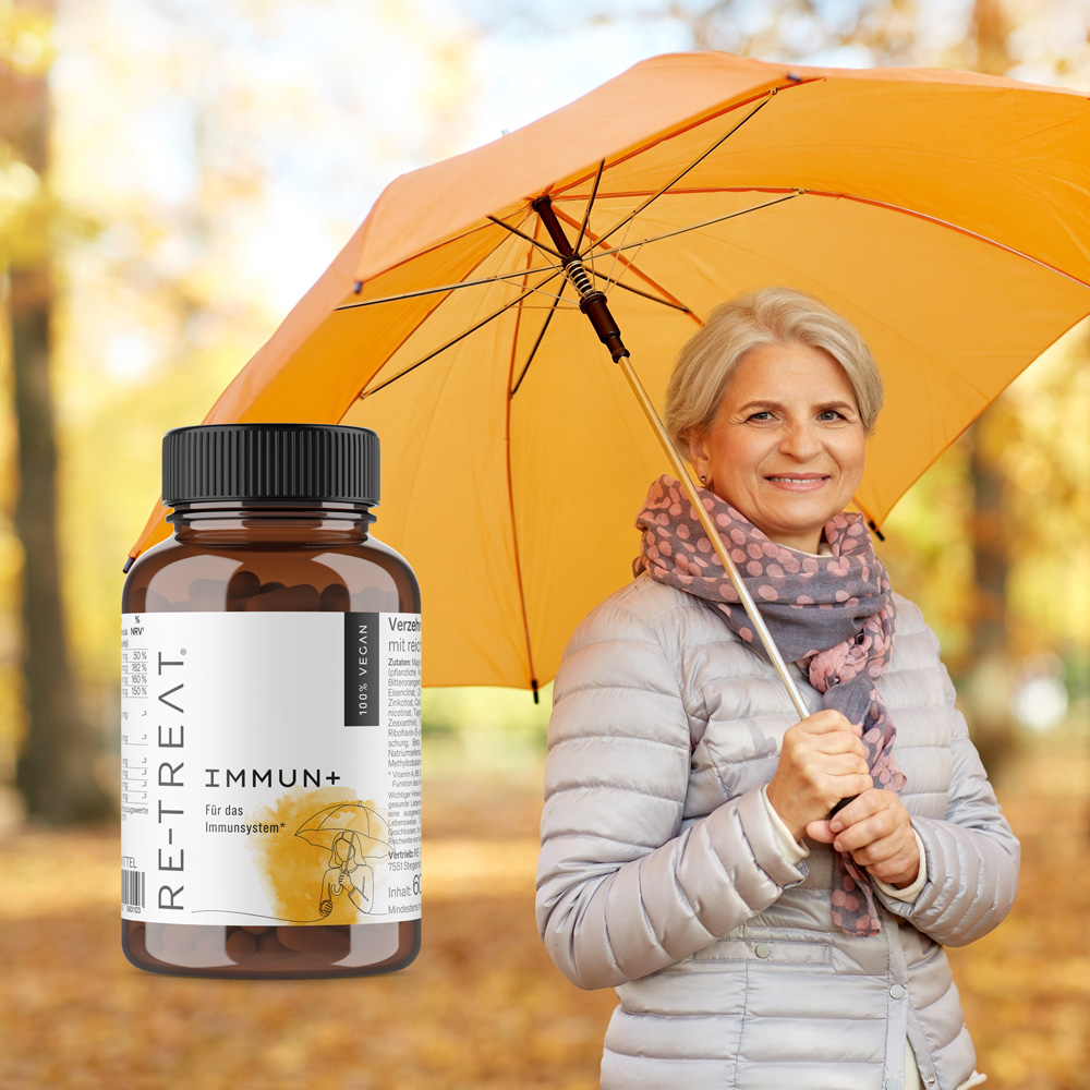 Ältere Dame steht unter gelben Regenschirm im Herbst mit Packshot von immun+ im Vordergrund